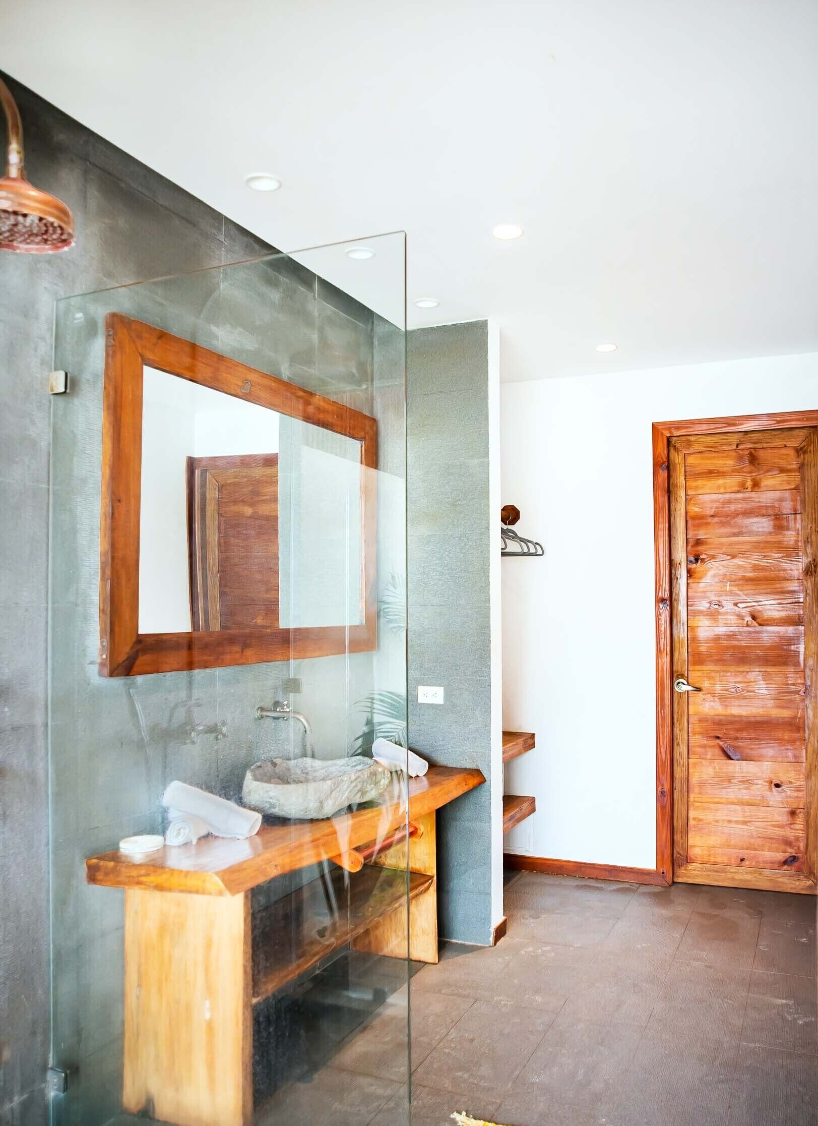 Ein modernes Badezimmer mit Glasabtrennung, Holzkosmetikschrank und großem Spiegel.