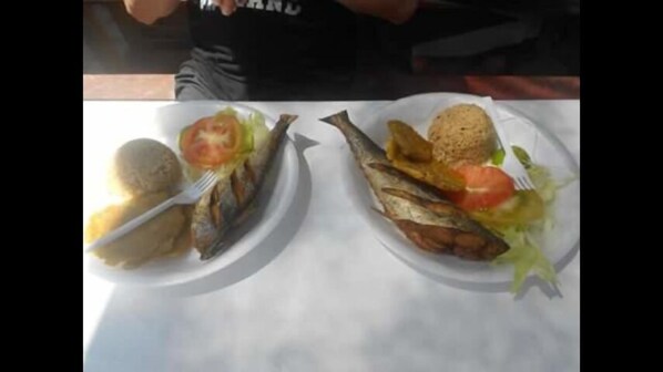 Two plates of food, one with a whole fish and a potato, and the other with a fish, a tomato, and a salad.