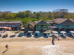 A beachside resort with thatched-roof huts, sun loungers, and umbrellas. - Hostal Lele (Cartagena)