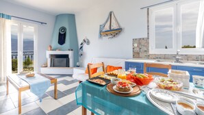 A bright room with a dining table set for breakfast, a fireplace, and a view of the outdoors. - Maistros Studios (Delphi)