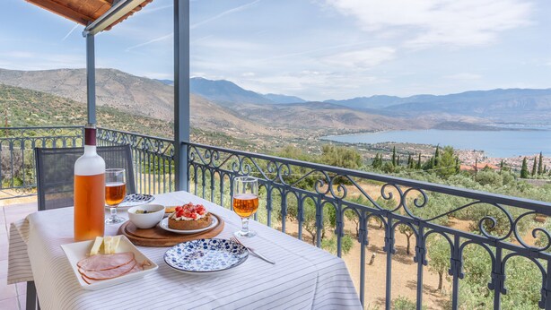 A table set with food and drinks on a balcony overlooking a mountainous landscape and a body of water. - Maistros Studios (Delphi)