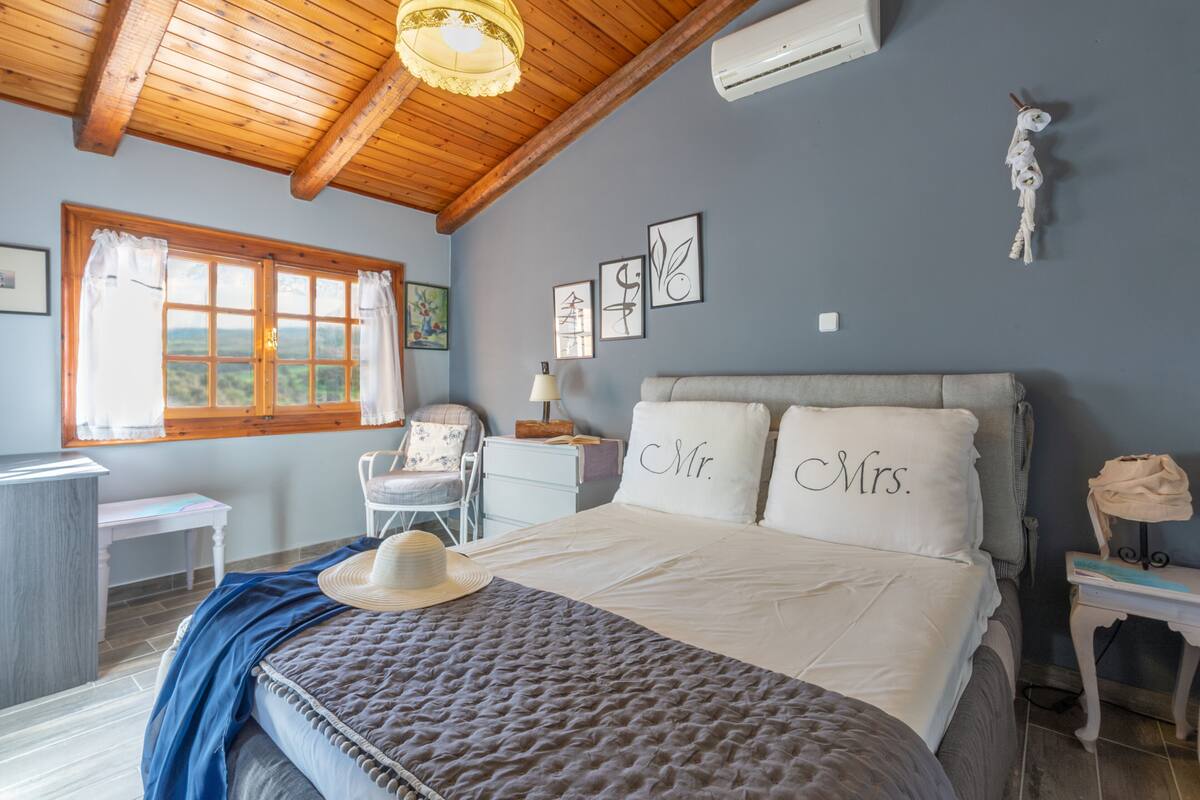A bedroom with a bed, a desk, a chair, and a window with curtains.