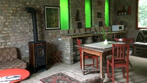 A rustic room with a stone wall, a fireplace, a wooden table with chairs, a red sofa, and a green-lit window. - Farmotel Stefania (Szakadat)