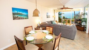 Een eetgedeelte met een glazen tafel, stoelen en uitzicht op de oceaan door grote ramen.