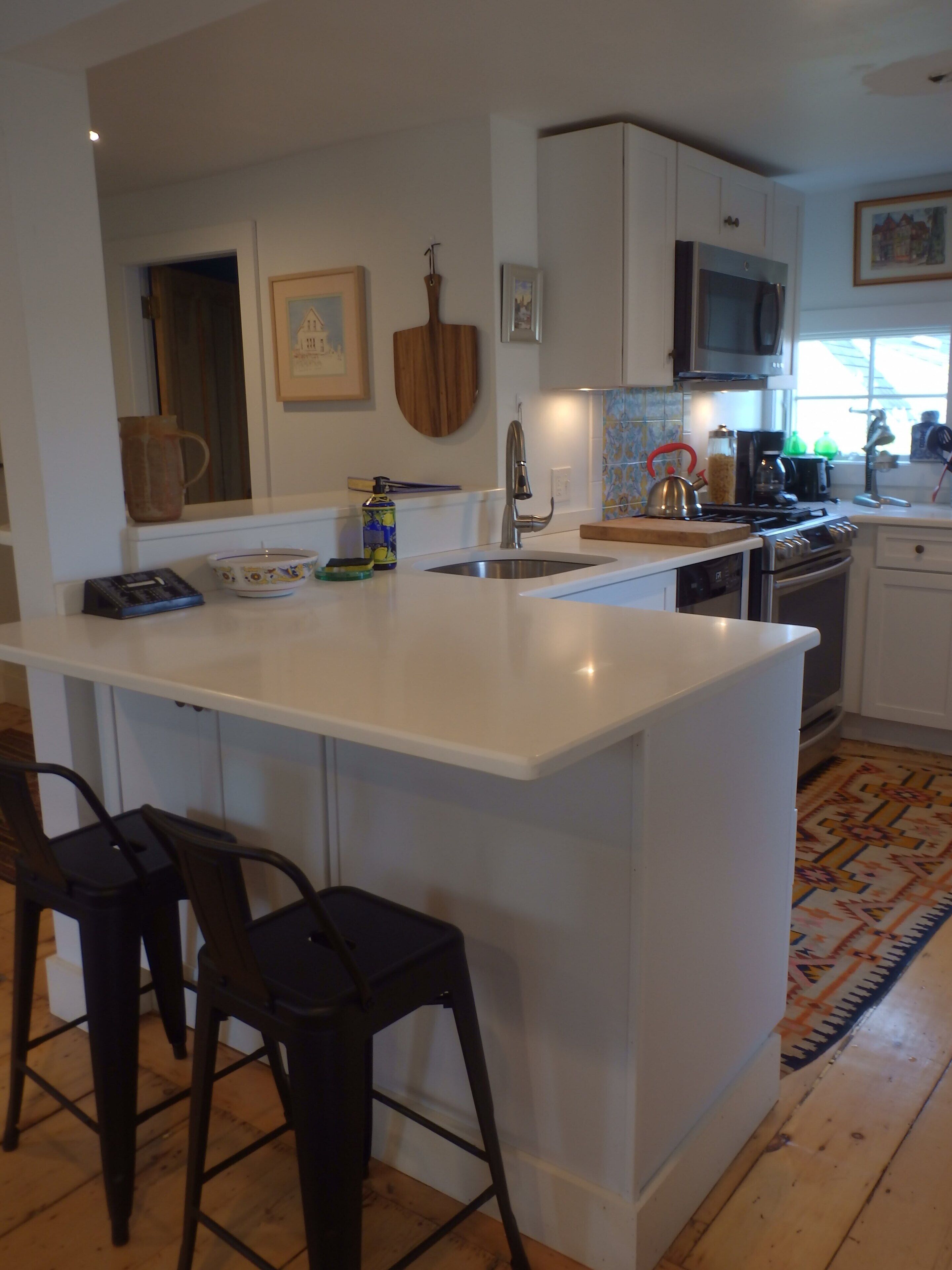 Una cocina moderna con una isla central, taburetes de bar, microondas, estufa y fregadero.