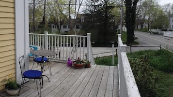 A wooden deck with outdoor seating, a white picket fence, and a road in the background.