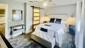 Un dormitorio con cama, banco, ventilador de techo y mesita de noche.