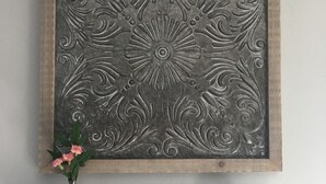Un panel metálico decorativo con diseño floral, colocado en la pared sobre una consola de madera con cajones.