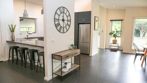 A modern kitchen with a central island, bar stools, a large wall clock, a refrigerator, and a dining area with a view. - DECKED OUT AT BRIGHT : Bright (Bright)