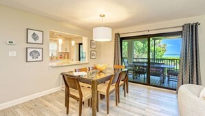 Un comedor con mesa y sillas, una cocina al fondo y un balcón con vistas al océano.