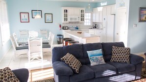 Uma sala de estar moderna com um sofá azul escuro, cadeiras de vime branco e uma mesa de jantar.