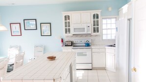Uma cozinha com armários brancos, micro-ondas, fogão e piso revestido de azulejos.