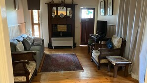 A living room with a sofa, chairs, a fireplace, a television, and a window with curtains. - Heritage, renovated, miners Cottage in Clunes (Clunes)