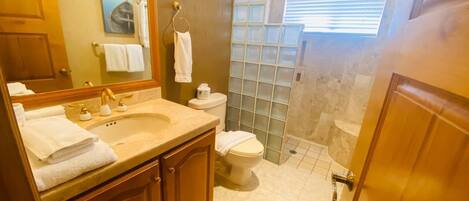A bathroom with a sink, mirror, toilet, and shower.