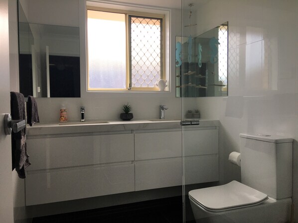 Un baño moderno con cabina de ducha de vidrio, inodoro, lavamanos con espejo y ventana con diseño de vidrio esmerilado.
