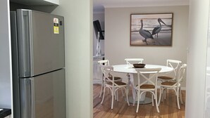 A modern kitchen with a stainless steel refrigerator, white cabinetry, and a dining area with a white table and chairs.