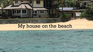 Ein zweistöckiges Strandhaus mit Balkon, umgeben von Palmen und mit Blick auf eine Bergkulisse.