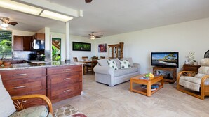 A spacious living area with a kitchen, dining table, sofa, and television. - Sunset Hale Kona: Ocean, Golf Course View, Keauhou Bay, Kona, Sleeps 4 (Kailua-Kona)
