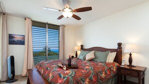 A hotel room with a bed, bedside tables, a ceiling fan, a bench, a window with curtains, and a view of the outdoors. - Sunset Hale Kona: Ocean, Golf Course View, Keauhou Bay, Kona, Sleeps 4 (Kailua-Kona)