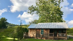 A rustic cabin with a metal roof, wooden walls, and a porch with chairs.