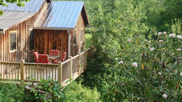 A wooden cabin with a balcony, red chairs, and a table.