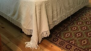A bed with a white bedspread and pillows, a wooden headboard, a green wall, a wooden wardrobe, a floor lamp, and a patterned rug.