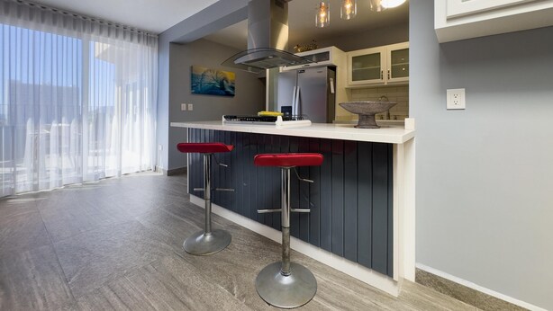 A modern kitchen with a bar area, bar stools, a refrigerator, and pendant lighting. - Mazatlan Casita del Cielo with Pool (Mazatlán)