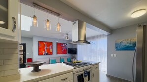 A modern kitchen with a central island, stainless steel appliances, pendant lighting, and artwork on the walls. - Mazatlan Casita del Cielo with Pool (Mazatlán)