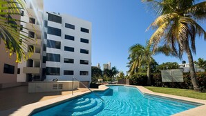 A swimming pool with a clear blue water feature, surrounded by a sandy area and palm trees. - Mazatlan Casita del Cielo with Pool (Mazatlán)