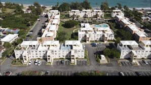 Luchtbeeld van een kustgebied met woongebouwen, een parkeerplaats en een strand op de achtergrond.