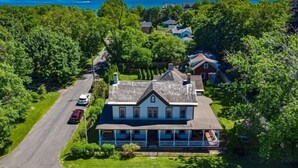Et stort hus med veranda og indkørsel, omgivet af træer og havudsigt.