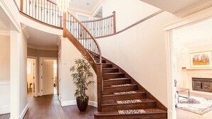 A wooden staircase with a railing, leading to a second floor. A large potted plant is placed near the staircase.