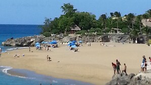 Ein Strand mit Menschen, Sonnenschirmen und einer felsigen Küstenlinie.