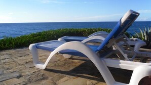 Eine Strandlounge mit weißen und blauen Liegestühlen mit Blick auf das Meer.