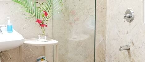 Un bagno con doccia vetrata, lavabo con specchio e ripiano con articoli da toilette.