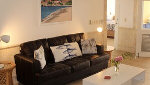 Ein Wohnzimmer mit einem schwarzen Ledersofa, einem weißen Couchtisch und einem Gemälde, das eine Strandansicht zeigt.