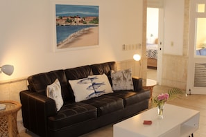 A living room with a black leather sofa, a white coffee table, and a painting of a beach scene on the wall.