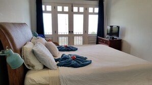 Ein Hotelzimmer mit Bett, Kissen, einem Fernseher und einem Balkon mit Rollläden.