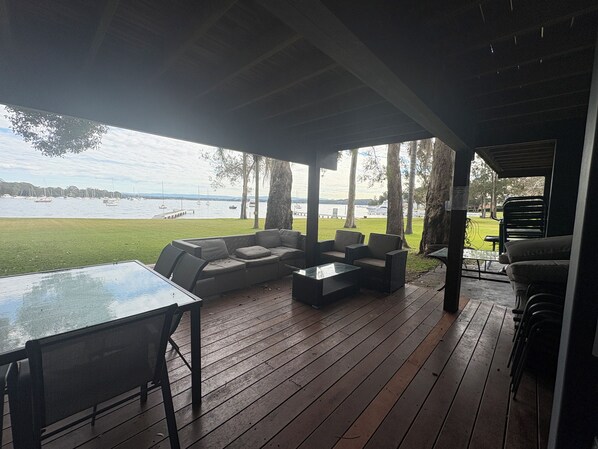 An outdoor deck with a sofa, chairs, and a table, overlooking a body of water with boats.