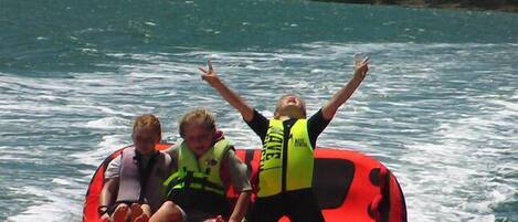 A red inflatable boat with two people wearing life jackets and one person standing with arms raised.