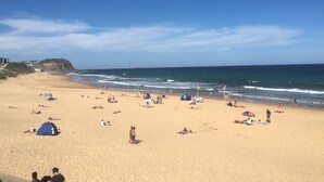 Ein weiter Sandstrand mit badenden und spazierenden Personen.