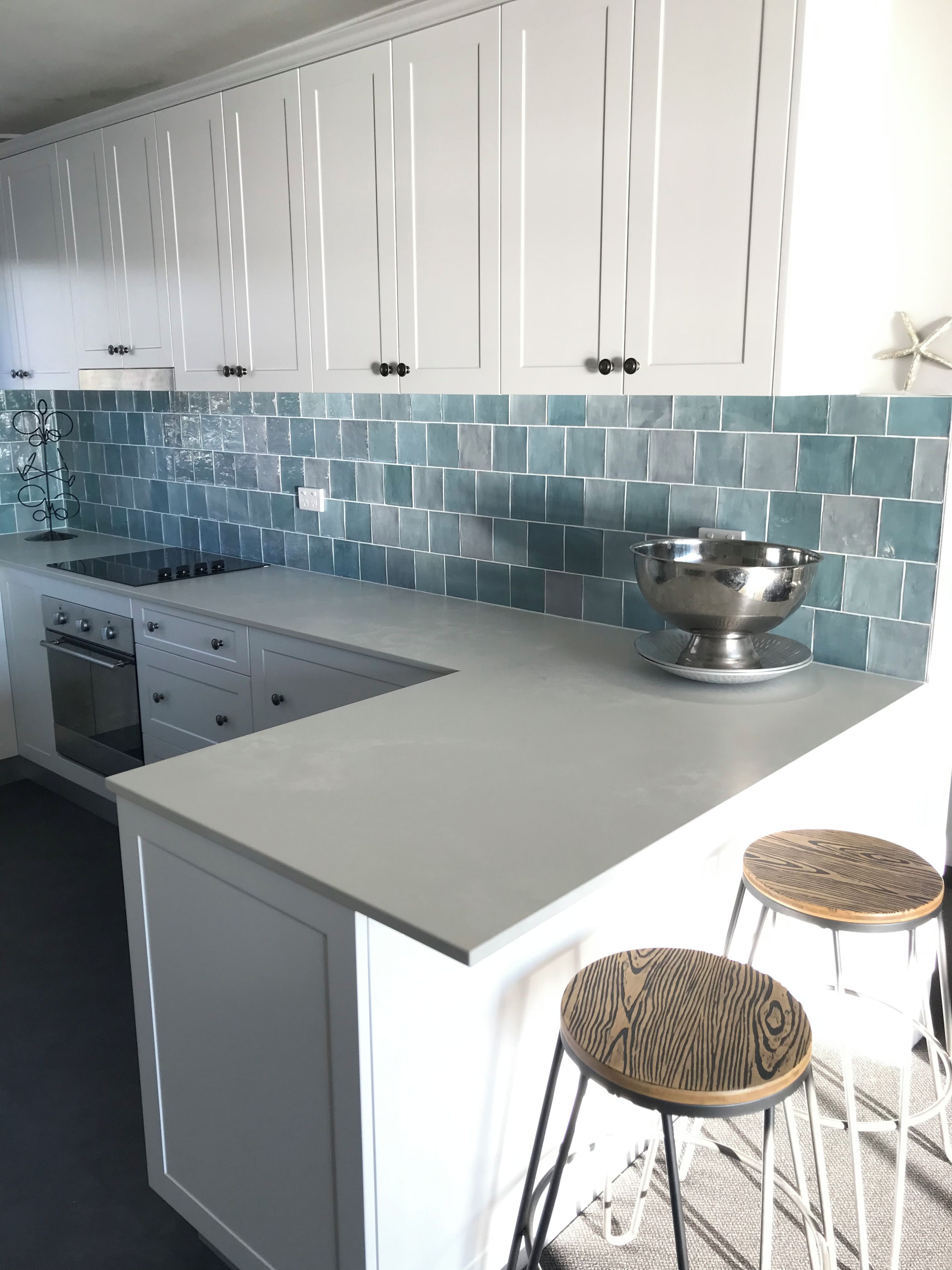 A modern kitchen with white cabinets, a blue-tiled backsplash, a stainless steel sink, and two bar stools.
