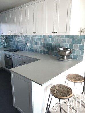 A modern kitchen with white cabinets, a blue-tiled backsplash, a stainless steel sink, and two bar stools.