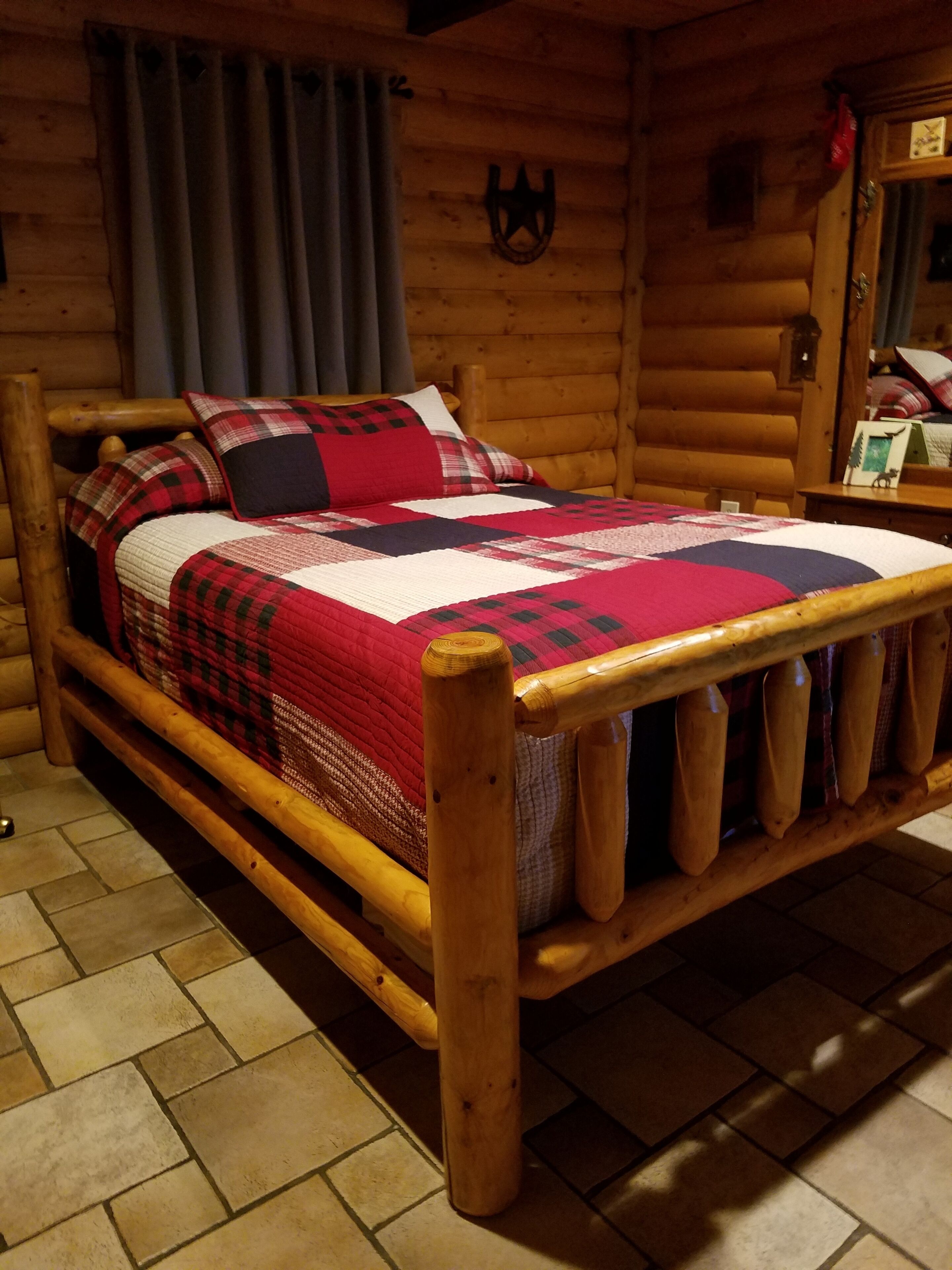Una cama de madera con colcha en una habitación tipo cabaña de troncos.