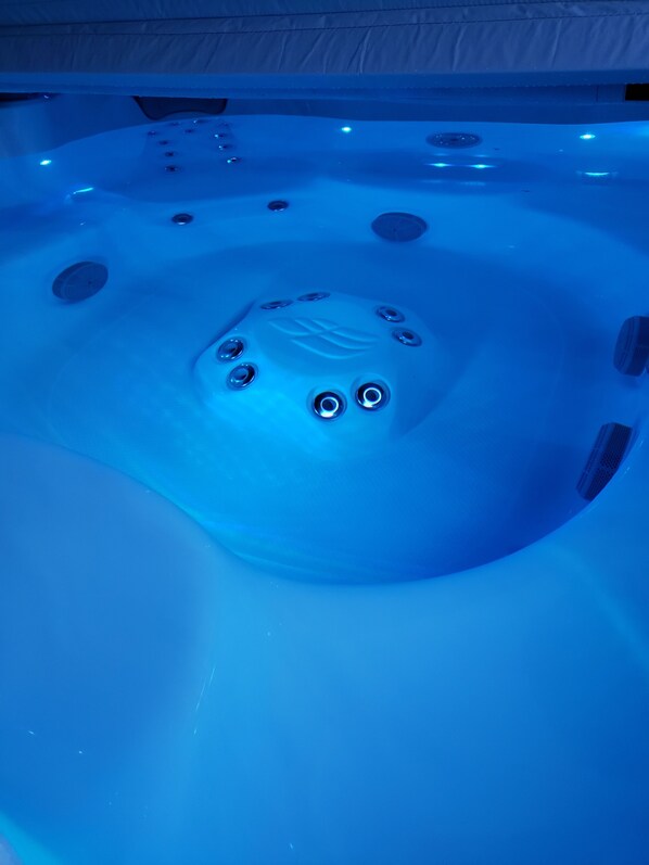 A hot tub with multiple jets and a central control panel, surrounded by a tiled floor.