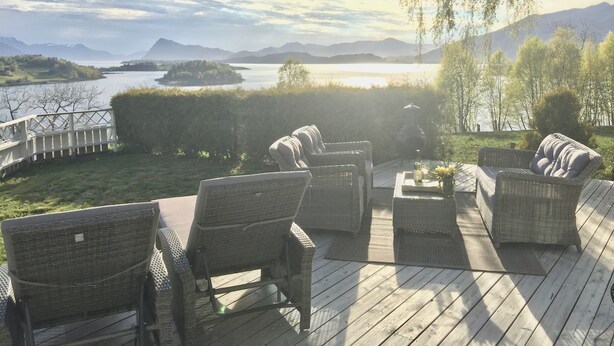 A deck with wicker furniture overlooking a lake and mountains. - Charming House with a Fantastic View of Norway's Nature (Ørsta)