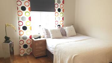 Quarto com cama, mesa de cabeceira, abajur e janela com cortina de bolinhas.