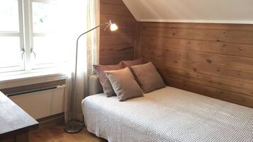 Una habitación acogedora con techo de madera, una cama con manta tejida, una lámpara de pie y una ventana con cortinas.