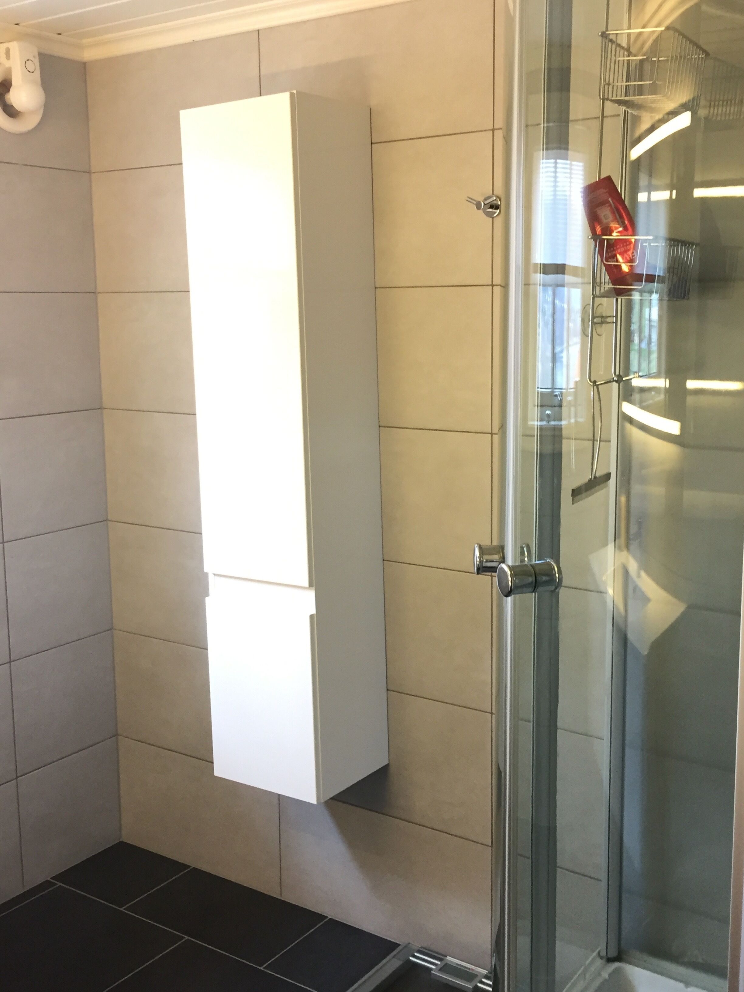 Une salle de bain avec une douche à parois de verre, un meuble blanc et un porte-serviettes sur lequel est posée une serviette rouge.