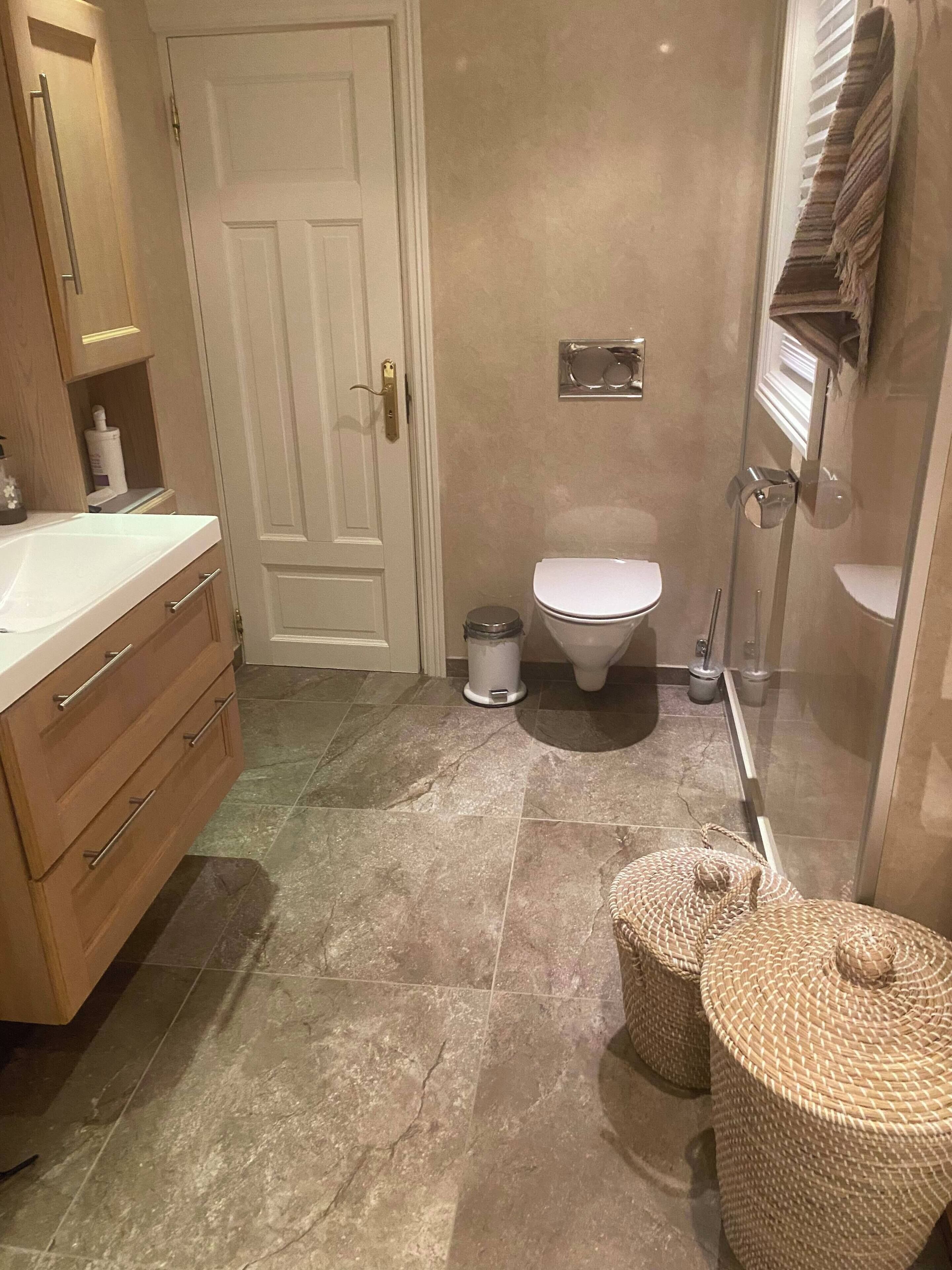 A bathroom with a white toilet, a sink with a mirror, wooden cabinets, and a tiled floor.